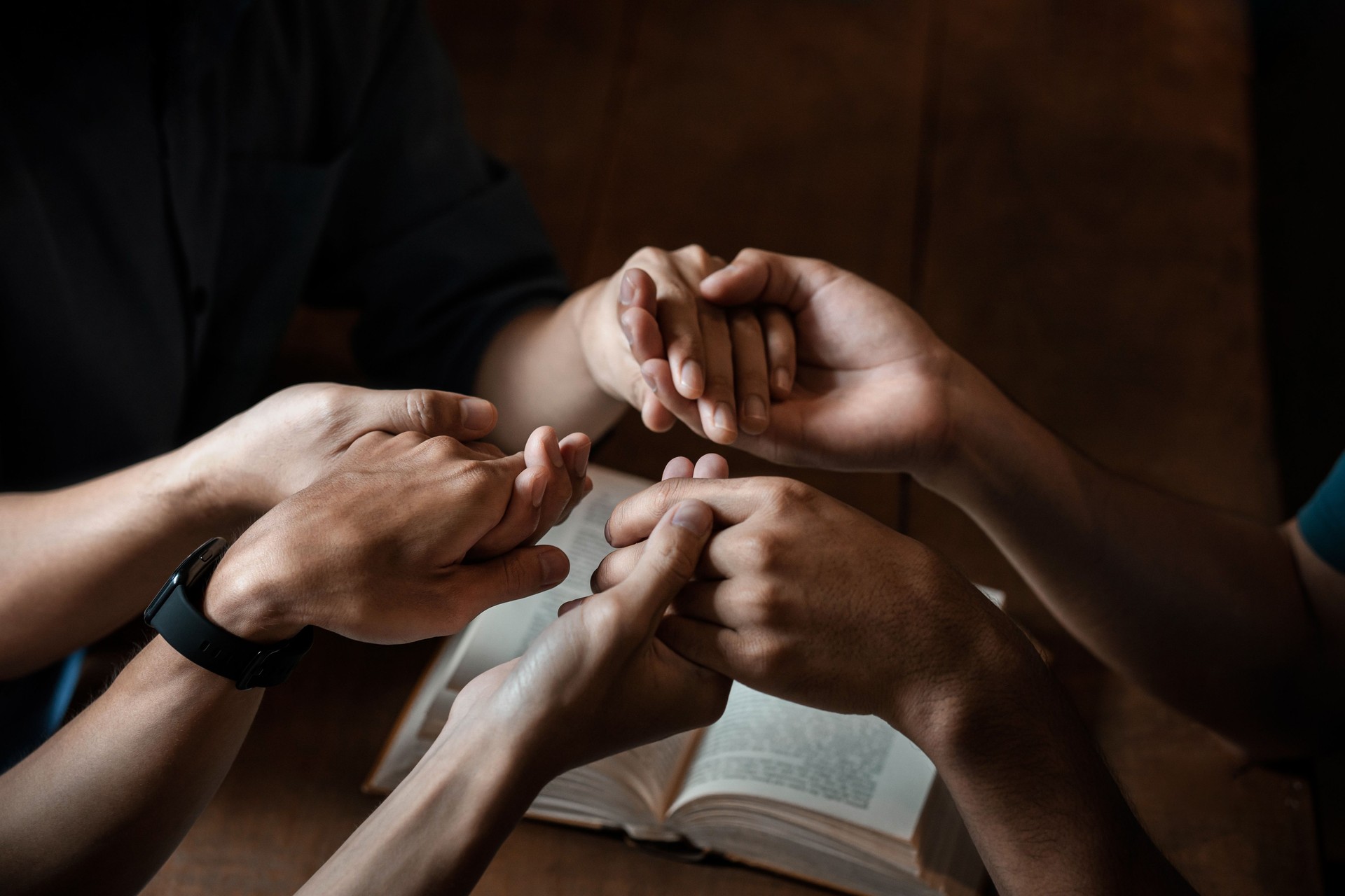 A group of young Christians holding hands in prayer for faith and scriptures on a wooden table as they pray to God. A group of young Christians holding hands in prayer for faith and scriptures on a wooden table as they pray to God.